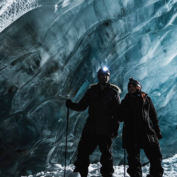 Two people wearing snow gear in a dark ice cave